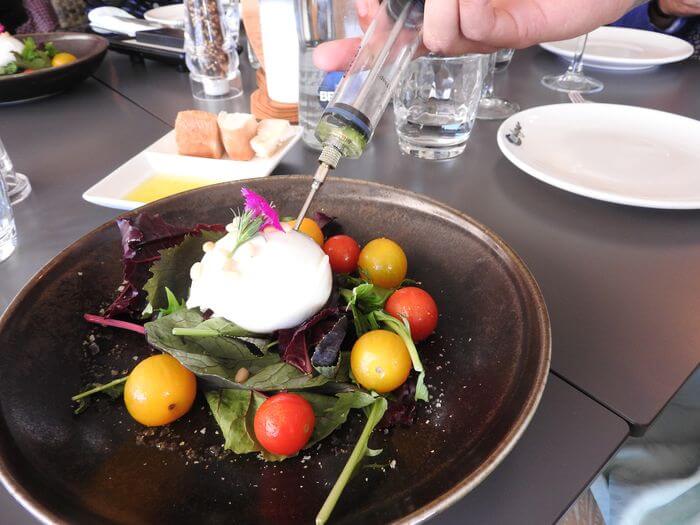 Burrata inyectada con pesto de rúcula, tomatitos del Baix Llobregat braseados y piñones tostados