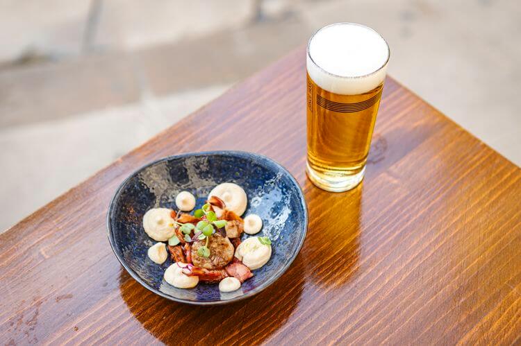 Marisco Barcelona – Hummus de judía blanca con butifarra de perol, crujiente de bacon y mermelada de cebolla caramelizada.